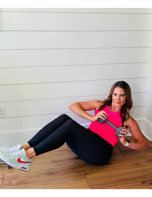 Woman exercising with a dumbbell on a wooden floor against a white wall.